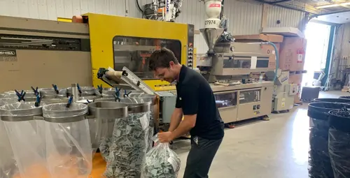 Jeune manœuvre emballant des sacs de pièces fabriquées par Plasti-Tom à l'intérieur de l'usine.