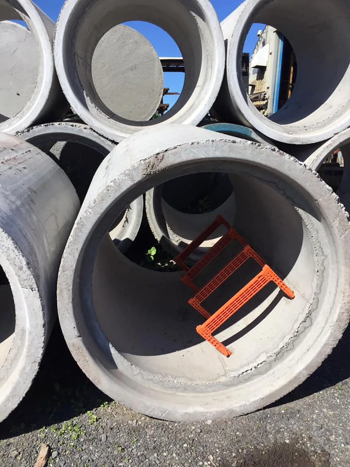 Tuyaux en béton empilés avec échelles oranges Plasti-Tom.