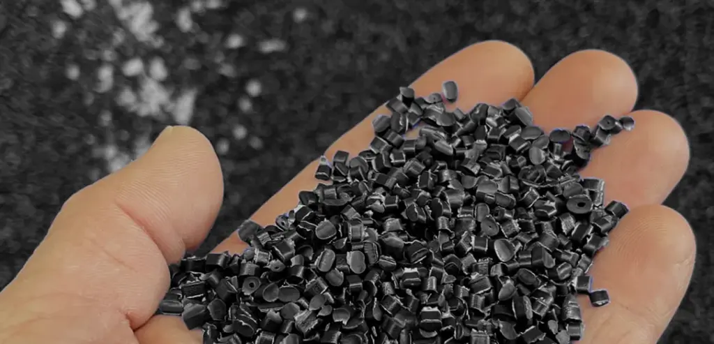 Main avec une poigné de granules de plastique noir Plasti-Tom.